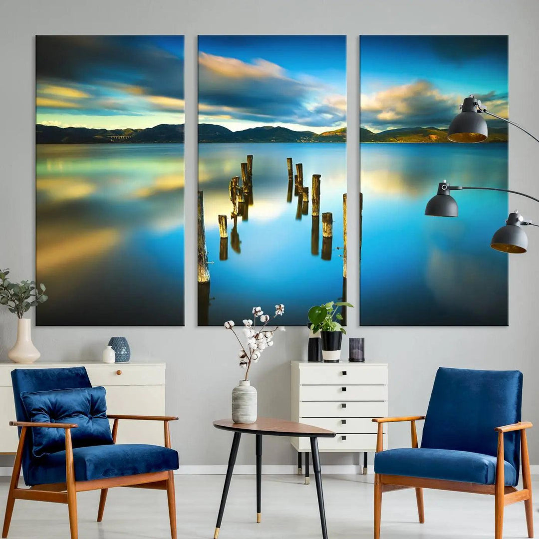 A triptych of a serene lake scene with old wooden pillars, blue sky, and clouds casts a coastal ambiance. The Sea Ocean Sunset Beach Wall Art Canvas Print reflects the soothing nature of the ocean.