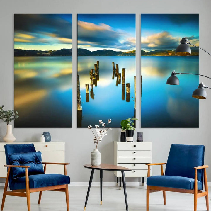 A triptych of a serene lake scene with old wooden pillars, blue sky, and clouds casts a coastal ambiance. The Sea Ocean Sunset Beach Wall Art Canvas Print reflects the soothing nature of the ocean.