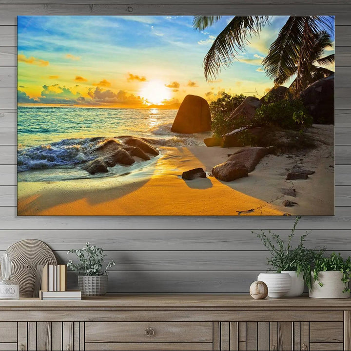 The Serene Tropical Beach Sunset Canvas Wall Art, a 3-panel giclee print, beautifully captures an ocean sunset with its depiction of palm trees and a coastal rock formation.