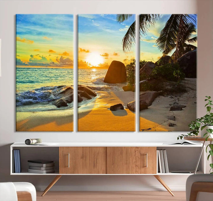 The Serene Tropical Beach Sunset Canvas Wall Art, a 3-panel giclee print, beautifully captures an ocean sunset with its depiction of palm trees and a coastal rock formation.