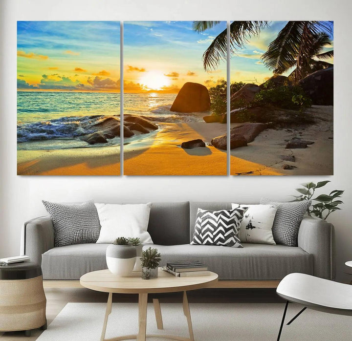 The Serene Tropical Beach Sunset Canvas Wall Art, a 3-panel giclee print, beautifully captures an ocean sunset with its depiction of palm trees and a coastal rock formation.