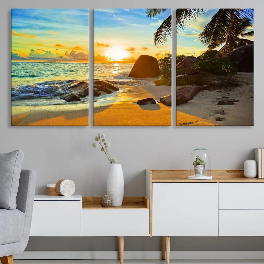 The Serene Tropical Beach Sunset Canvas Wall Art, a 3-panel giclee print, beautifully captures an ocean sunset with its depiction of palm trees and a coastal rock formation.