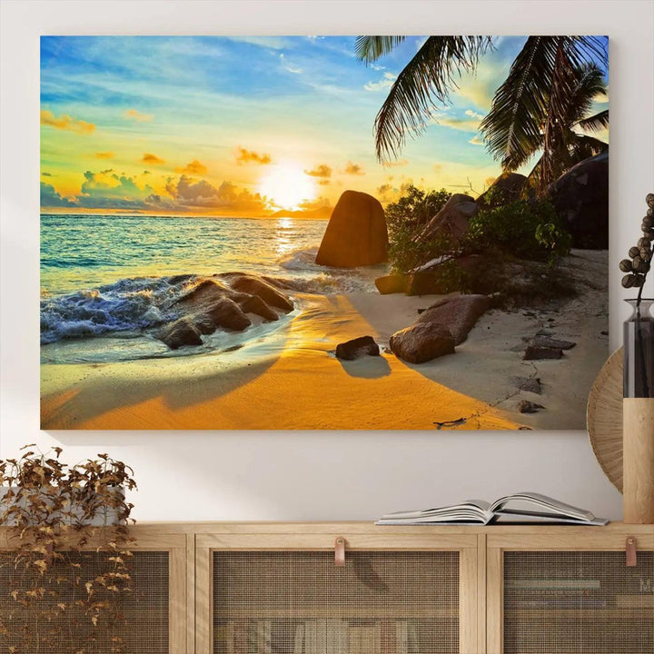 The Serene Tropical Beach Sunset Canvas Wall Art, a 3-panel giclee print, beautifully captures an ocean sunset with its depiction of palm trees and a coastal rock formation.