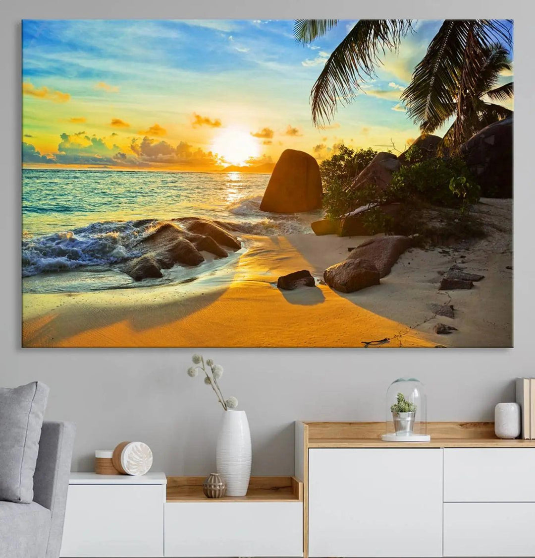 The Serene Tropical Beach Sunset Canvas Wall Art, a 3-panel giclee print, beautifully captures an ocean sunset with its depiction of palm trees and a coastal rock formation.