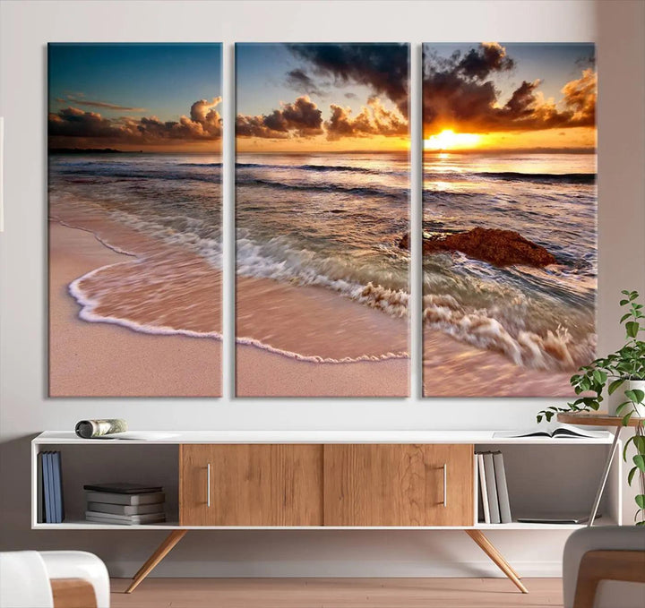 The Sunset Beach Waves Triptych Wall Art, featuring a tropical ocean scene on giclee canvas with a gallery wrap, adorns the wall in a cozy, coastal-themed living room.