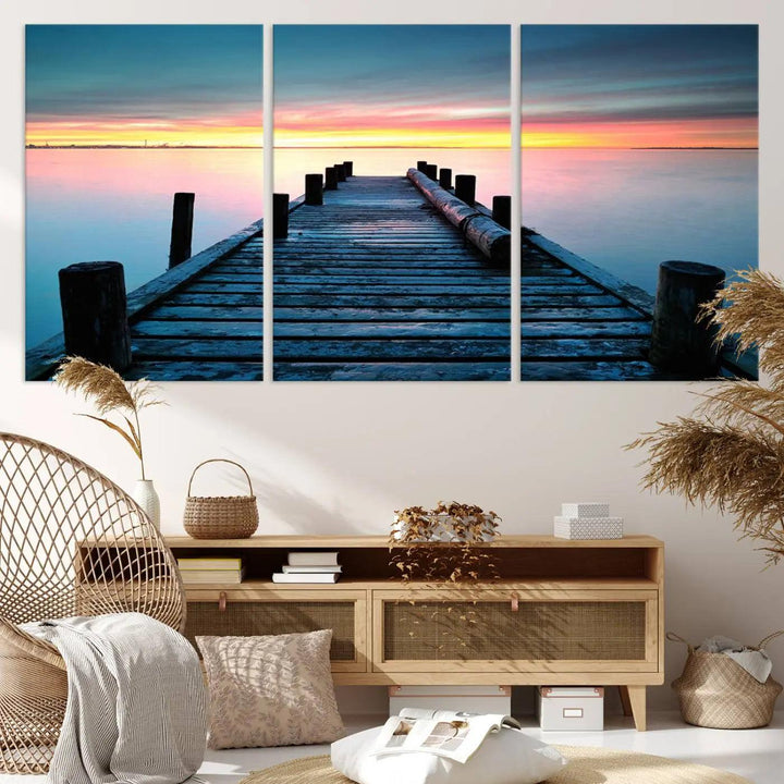 The "Sunset Pier Triptych Canvas Art," a giclee print known for its Canon print quality and gallery wrap finish, captures a wooden pier stretching into a tranquil lake at sunset beneath vibrant orange and blue skies. It makes an ideal centerpiece for coastal-themed art settings.