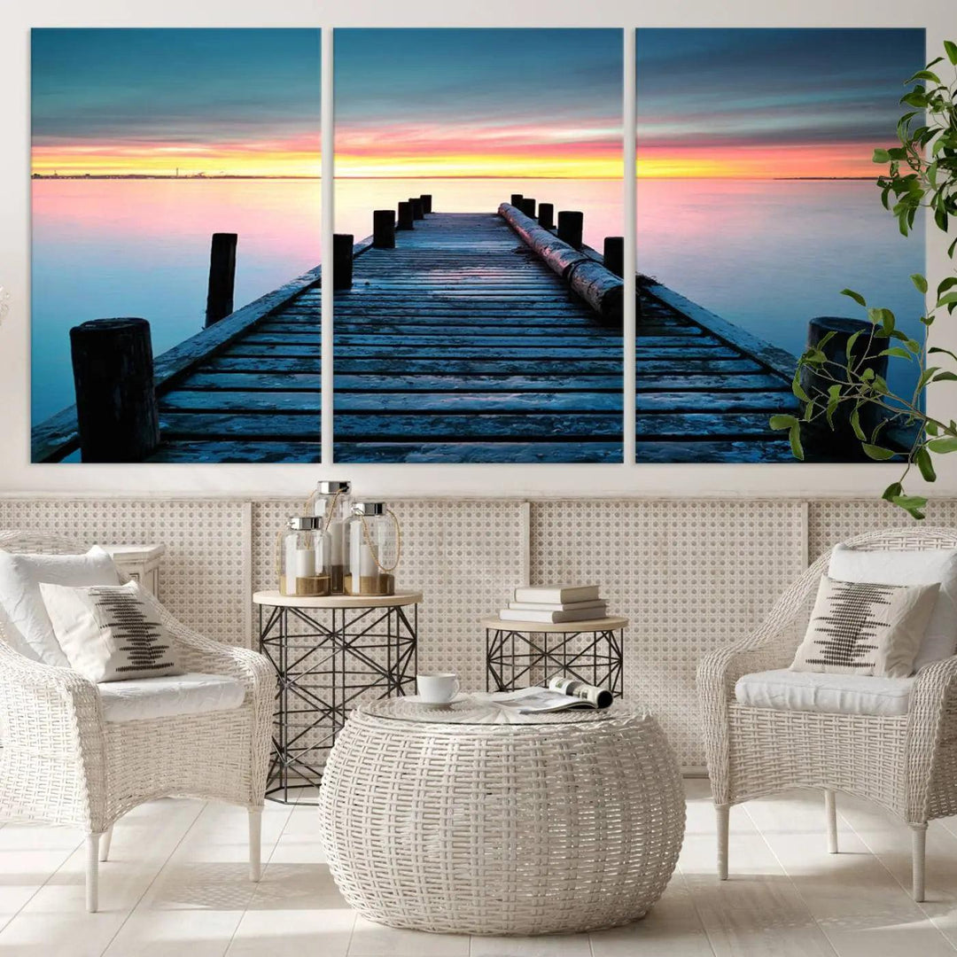 The "Sunset Pier Triptych Canvas Art," a giclee print known for its Canon print quality and gallery wrap finish, captures a wooden pier stretching into a tranquil lake at sunset beneath vibrant orange and blue skies. It makes an ideal centerpiece for coastal-themed art settings.