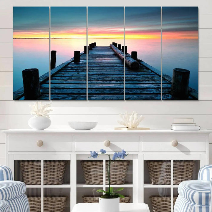 The "Sunset Pier Triptych Canvas Art," a giclee print known for its Canon print quality and gallery wrap finish, captures a wooden pier stretching into a tranquil lake at sunset beneath vibrant orange and blue skies. It makes an ideal centerpiece for coastal-themed art settings.