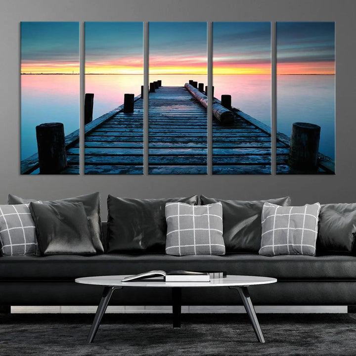 The "Sunset Pier Triptych Canvas Art," a giclee print known for its Canon print quality and gallery wrap finish, captures a wooden pier stretching into a tranquil lake at sunset beneath vibrant orange and blue skies. It makes an ideal centerpiece for coastal-themed art settings.