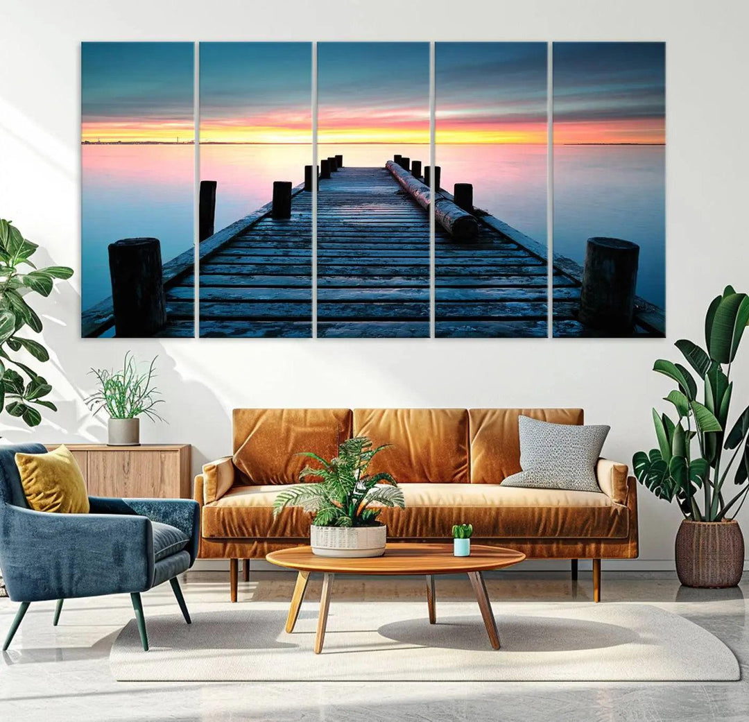 The "Sunset Pier Triptych Canvas Art," a giclee print known for its Canon print quality and gallery wrap finish, captures a wooden pier stretching into a tranquil lake at sunset beneath vibrant orange and blue skies. It makes an ideal centerpiece for coastal-themed art settings.