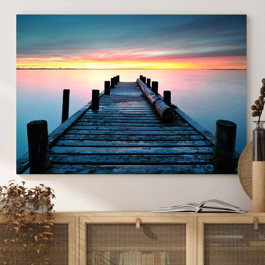 The "Sunset Pier Triptych Canvas Art," a giclee print known for its Canon print quality and gallery wrap finish, captures a wooden pier stretching into a tranquil lake at sunset beneath vibrant orange and blue skies. It makes an ideal centerpiece for coastal-themed art settings.