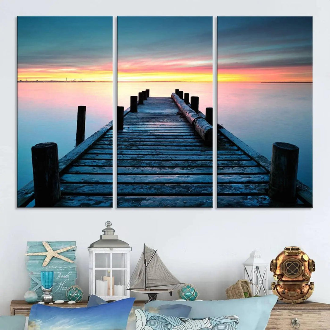 The "Sunset Pier Triptych Canvas Art," a giclee print known for its Canon print quality and gallery wrap finish, captures a wooden pier stretching into a tranquil lake at sunset beneath vibrant orange and blue skies. It makes an ideal centerpiece for coastal-themed art settings.