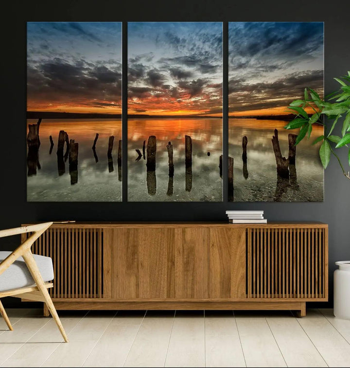 The "Sunset Reflection on Wooden Pier Giclee Canvas Print" is a panoramic wall art piece showcasing serene nature photography with a colorful sunset over water and wooden posts.