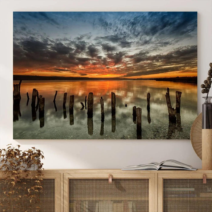 The "Sunset Reflection on Wooden Pier Giclee Canvas Print" is a panoramic wall art piece showcasing serene nature photography with a colorful sunset over water and wooden posts.