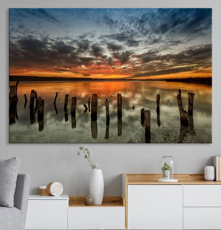 The "Sunset Reflection on Wooden Pier Giclee Canvas Print" is a panoramic wall art piece showcasing serene nature photography with a colorful sunset over water and wooden posts.