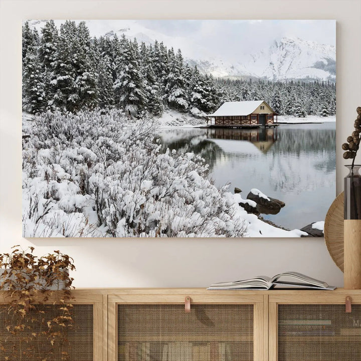 Experience the beauty of winter with the "Cabin by the Lake Canvas Wall Art," showcasing a serene snowy landscape. This rustic nature decor features a cozy cabin nestled amid snow-laden trees, set against a breathtaking mountain view, perfect for enhancing your living room.